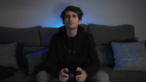 young man playing video games at home with a blue light in the background, medium shot