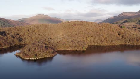 Imágenes-Aéreas-De-Drones-De-Un-Amanecer-De-Otoño-Sobre-Las-Montañas-Ben-Lomond-Y-Beinn-Bhreac-En-Loch-Lomond-Y-El-Parque-Nacional-Trossachs,-Escocia-Con-Bosques-Nativos-De-Hoja-Ancha-En-La-Costa-De-Loch-Lomond