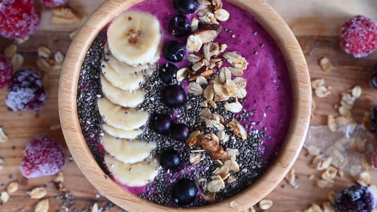 Primo piano di una bowl di açaí con frutta e semi su un vassoio di legno con frutta congelata sopra
