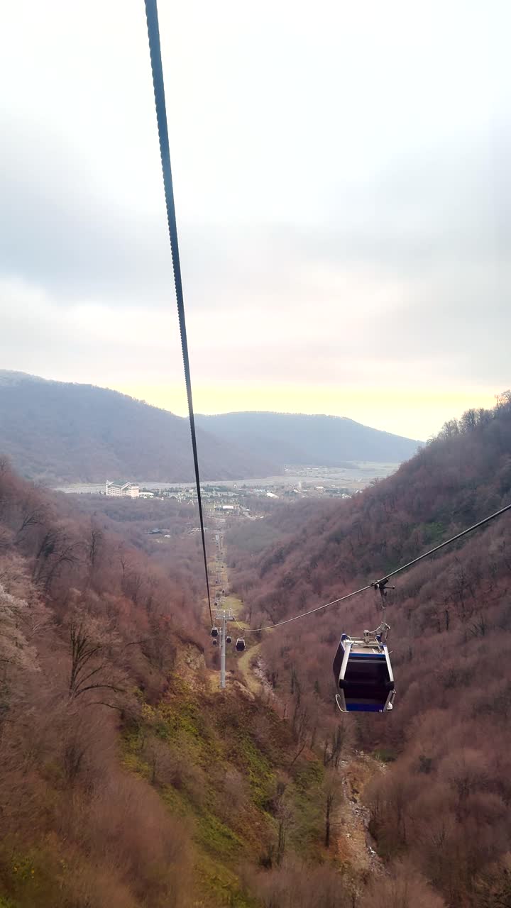 Cable car gliding over Shahdag’s forested valley with mountain views and distant townscape. Shahdag, Azerbaijan