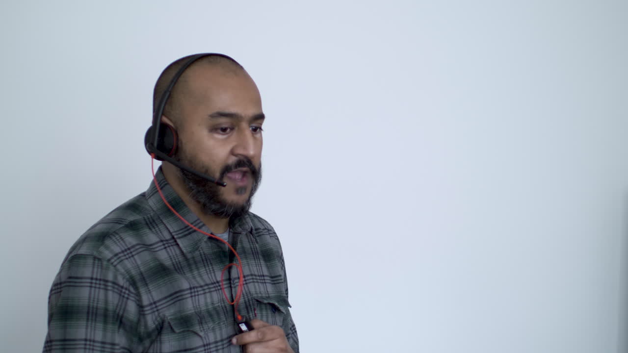 macho calvo de minorías étnicas tomando llamada en auriculares contra la pared blanca