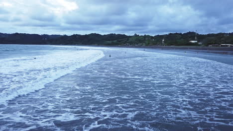 aerial-view-of-sea-waves-passing-by-and-swimmers-trees-and-beach