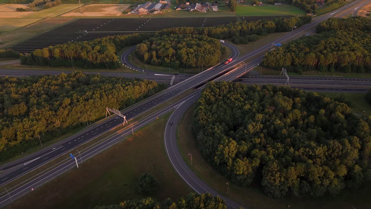 Aerial view of a highway interchange surrounded by forest and a solar panel field at sunset