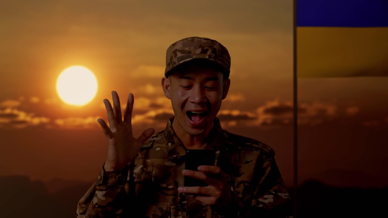 우크라이나 국기를 배경으로 해가 지는 동안 스마트폰을 사용하는 군인