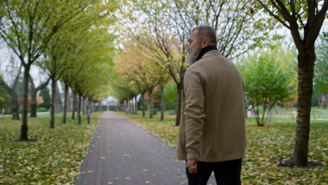 Back-view-man-walking-across-beautiful-park-in-autumn.-Rear-view-of-senior.