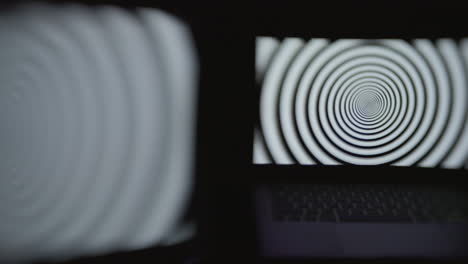 two computer screens in a dark room displaying a hypnotic spiral pattern