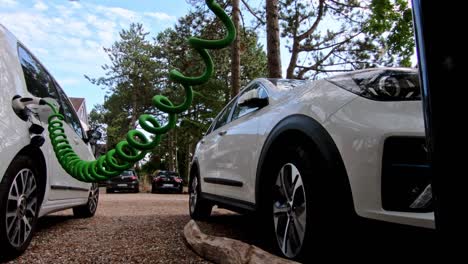 dos autos ev blancos conectados a una estación de carga pública en un bosque