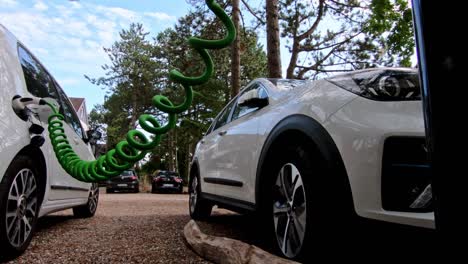 two white ev cars plugged into a public charging station in a forest