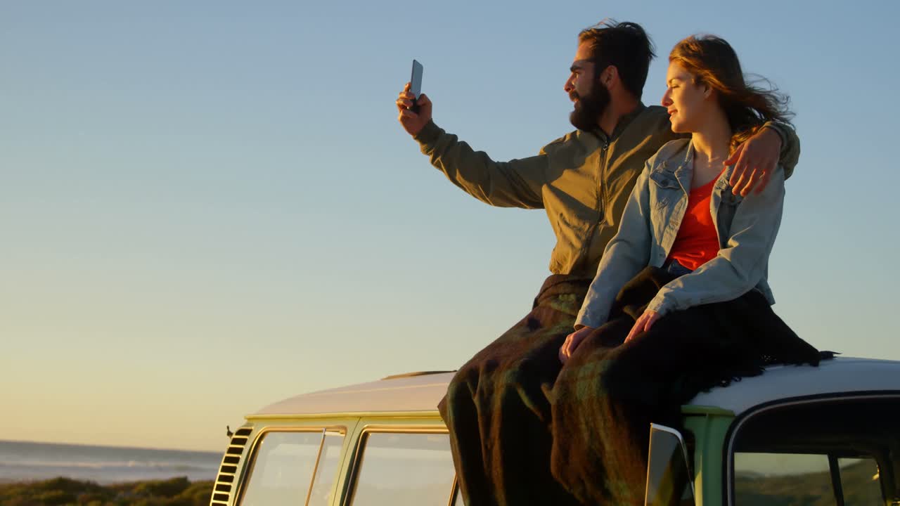 pareja tomando una selfie durante la puesta de sol en la playa 4k