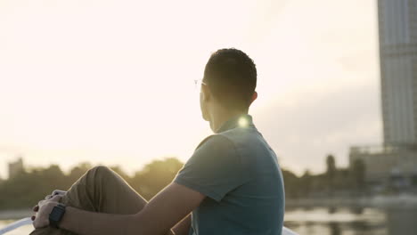 Circling-man-sitting-on-bow-of-boat-watching-sunrise-peacefully,-slow-motion