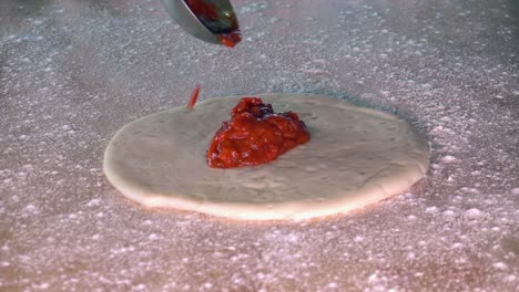 tomato sauce being spread on a pizza dough base