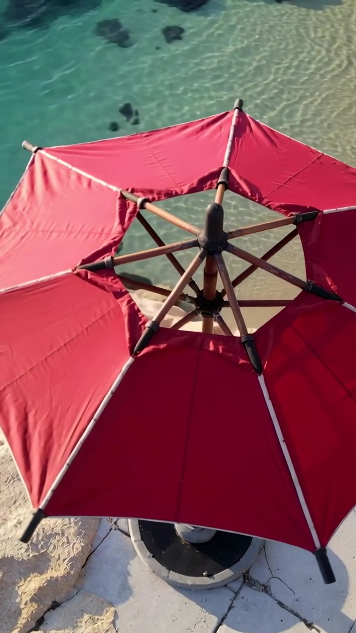 Video verticale: La telecamera si allontana, mostrando un ombrellone ottagonale rosso su una piattaforma per rivelare la costa.