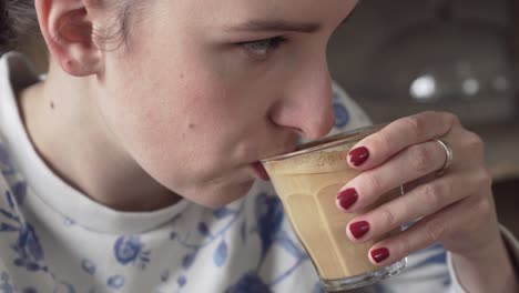 young beautiful woman drinking flat white coffee, picking up glass from a wooden table