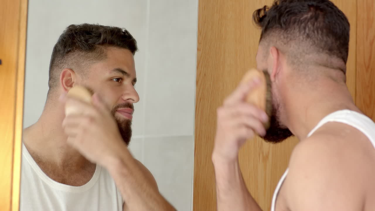 Grooming beard, man brushing facial hair while looking in bathroom mirror
