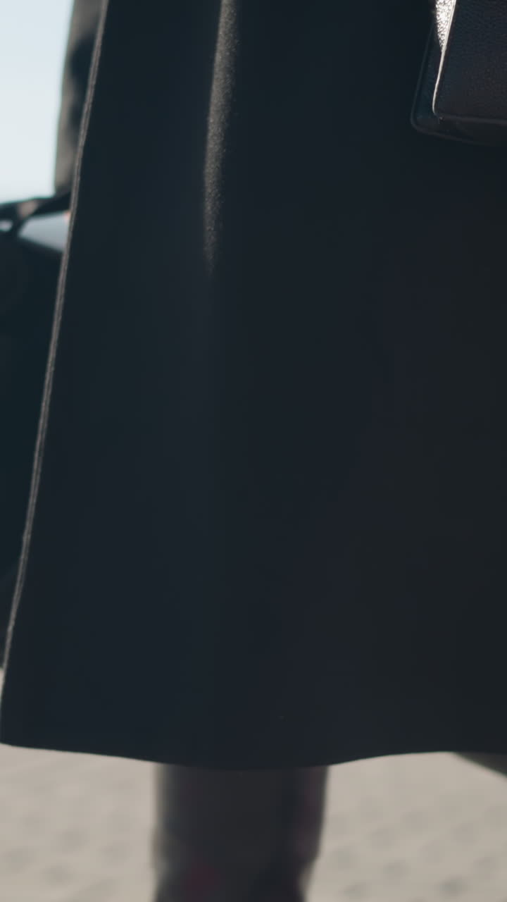 primer plano de botas de cuero y detalles de abrigos fluidos, capturando movimiento y elegancia con medias transparentes en una calle urbana, el fondo incluye movimiento borroso de automóviles y arquitectura moderna