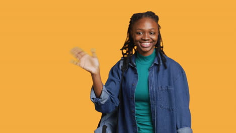 Cheerful-student-witch-school-rucksack-doing-greeting-hand-gesture