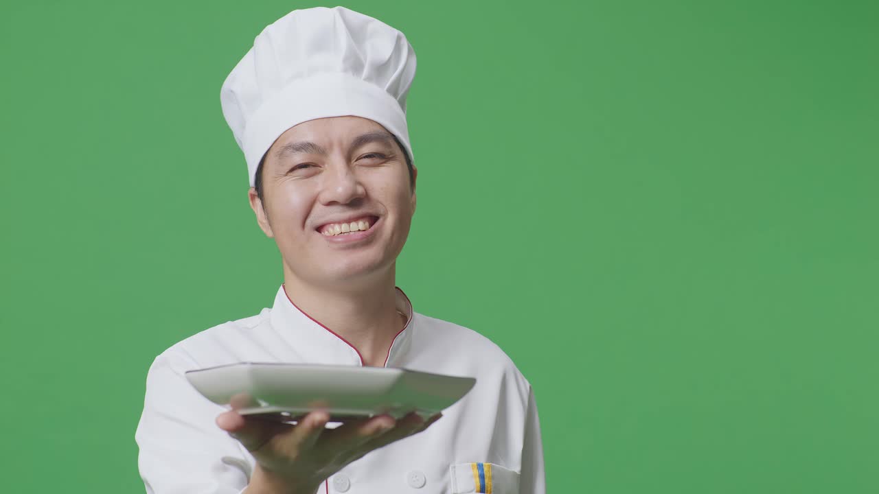 Close Up Of Asian Man Chef Smiling And Giving A Dish To Camera While Standing In The Green Screen Background Studio