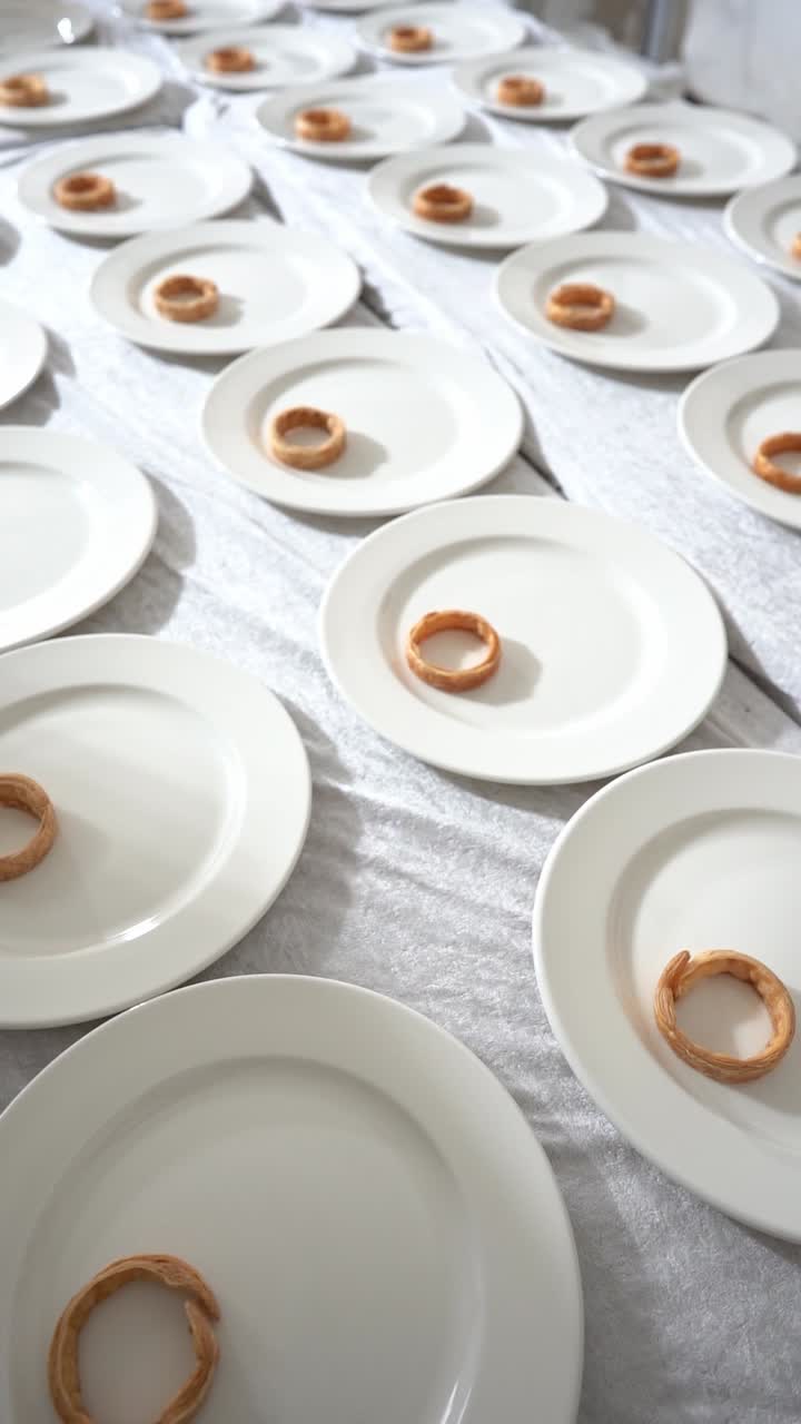 Minimalist fine dining setup with white plates arranged in rows, each holding a small pastry, close up shot