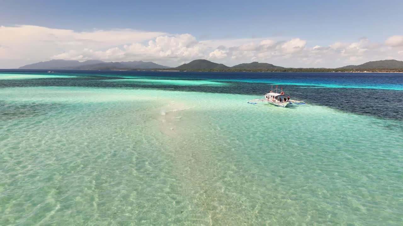 A boat glides across the shallow turquoise waters of Candaraman Sand Bar, with distant green islands and blue skies in the background, highlighting the tropical beauty of Balabac, Palawan, Philippines