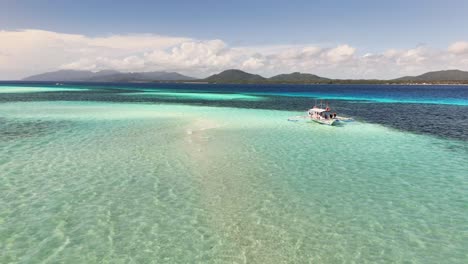a boat glides across the shallow turquoise waters of candaraman sand bar, with distant green islands and blue skies in the background, highlighting the tropical beauty of balabac, palawan, philippines