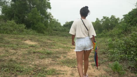 Young-Indian-woman-is-walking-into-the-woods-holding-an-umbrella-in-hand