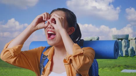 close up of asian female hiker with mountaineering backpack making binoculars gesture looking at something then saying wow while traveling in stonehenge