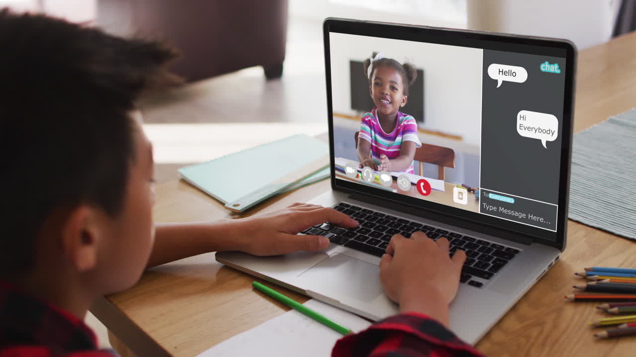 Schoolboy using laptop for online lesson at home, with schoolgirl and webchat on screen