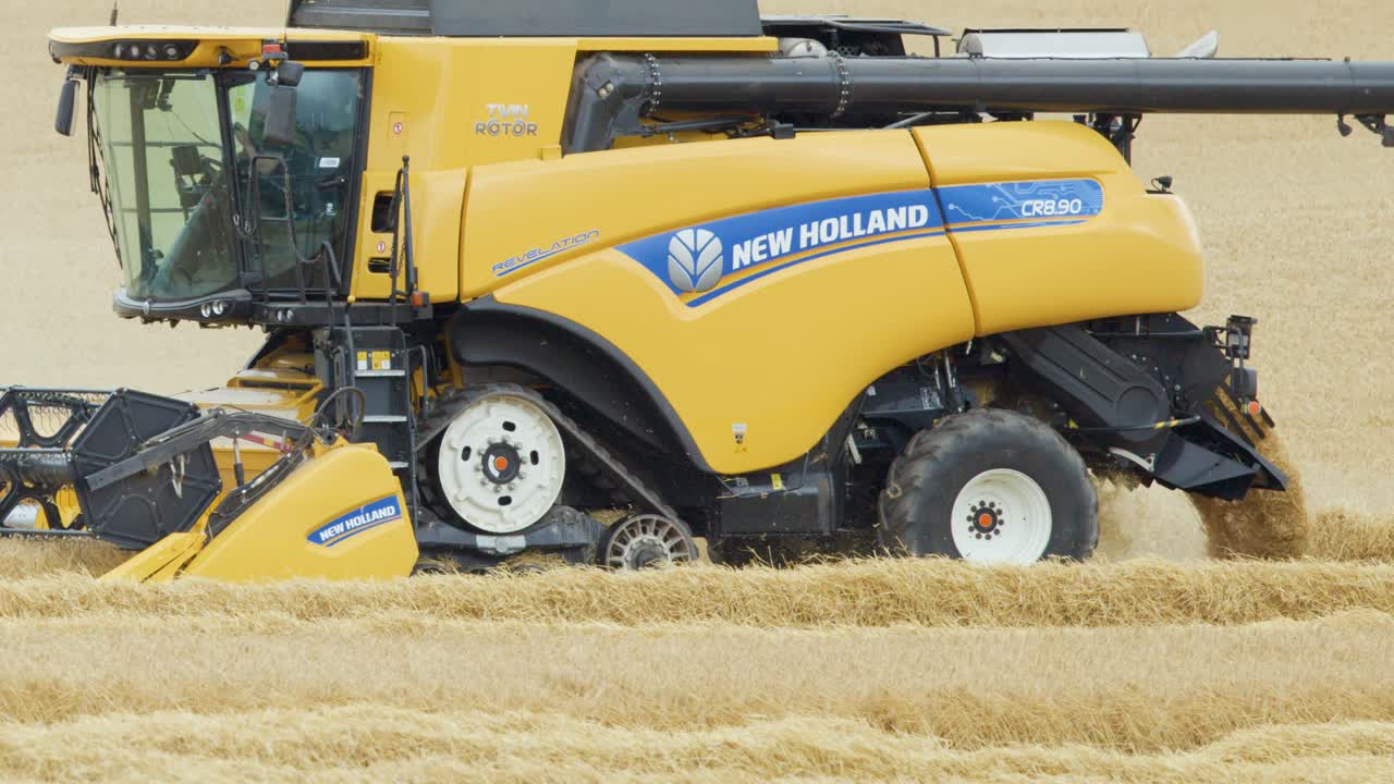 A large yellow combine harvester moves steadily through a golden wheat field under soft daylight, capturing the crop harvesting process with a smooth side tracking shot