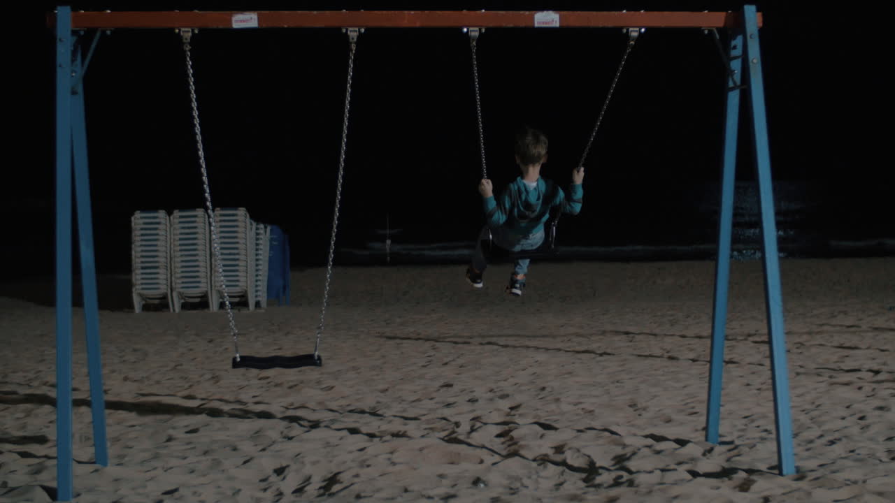 niño solitario balanceándose en la playa por la noche