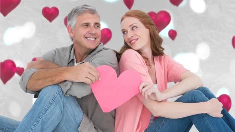 pareja sentada y sosteniendo un corazón rosado