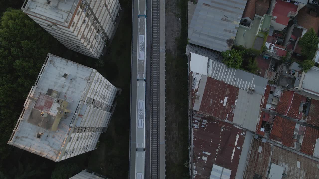 Riprese aeree dall'alto che seguono un treno in movimento tra gli edifici e le case del quartiere di Belgrano, Buenos Aires, Argentina.