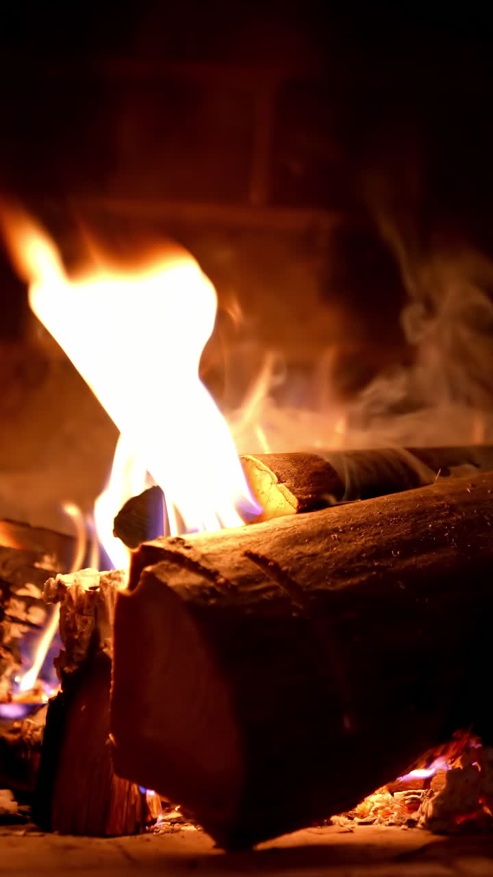 Wooden logs in fire on brick fireplace background. Wood burning in fire flame. Cozy warm fireplace in a country house. Close-up. Vertical video