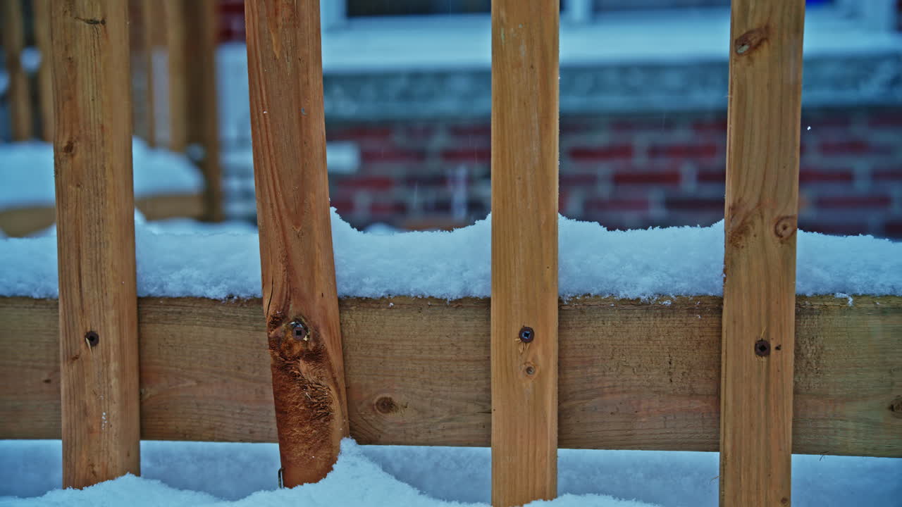 First snow gently accumulating along a backyard deck fence as snow falls during an early seasonal transition, creating a calm and minimal background. Lateral movement
