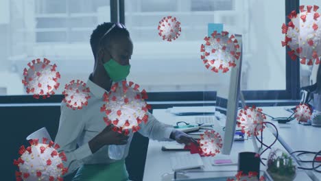 animación de células de virus sobre una mujer de negocios con máscara facial desinfectando la computadora en la oficina