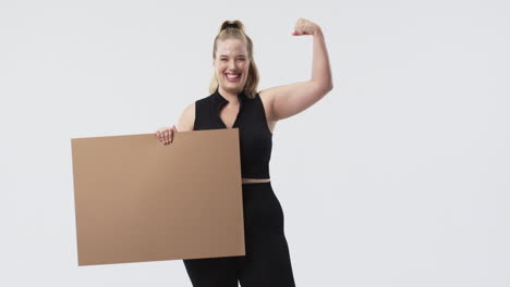 young caucasian plus size woman with blonde hair smiling and holding blank brown sign