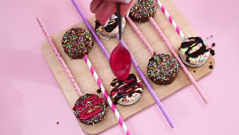 decorating delicious cake pops with pink strawberry syrup. making cake pops dessert on wooden board on pastel pink theme