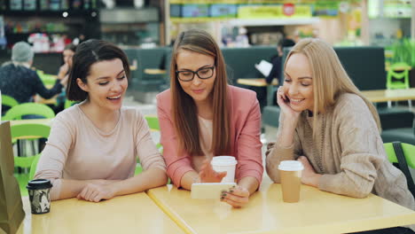 three women friends enjoying coffee and social media at a shopping mall food court