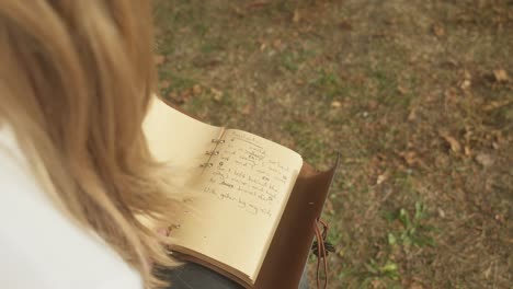 over shoulder shot young blonde woman writes poetic lyrics in book