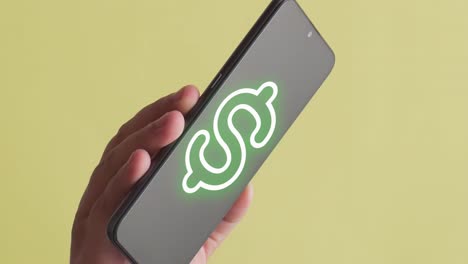 Person-holding-a-mobile-phone-where-the-animation-of-green-dollar-symbol-appears,-yellow-background