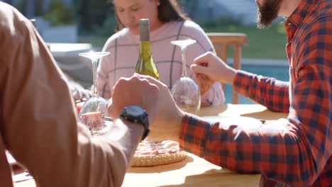 Happy-diverse-male-and-female-friends-saying-prayer-on-thanksgiving-celebration-meal-in-sunny-garden