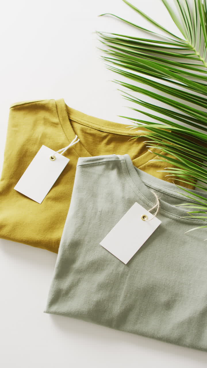 Vertical video of close up of green and mustard folded t shirts with tags with copy space