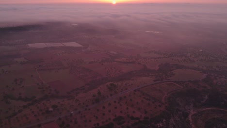 Italian-countryside-during-misty-morning-colorful-sunrise,-sun-on-horizon,-aerial