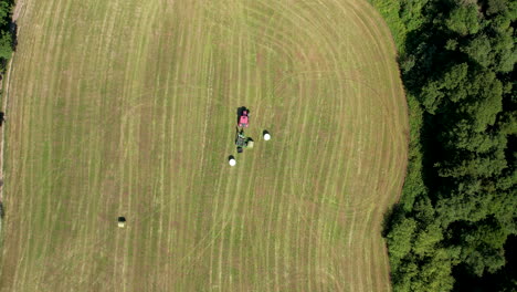 Roter-Traktor-Sammelt-Und-Rollt-Heu-Nach-Der-Ernte-Im-Landwirtschaftlichen-Bereich---Luft-Von-Oben-Nach-Unten