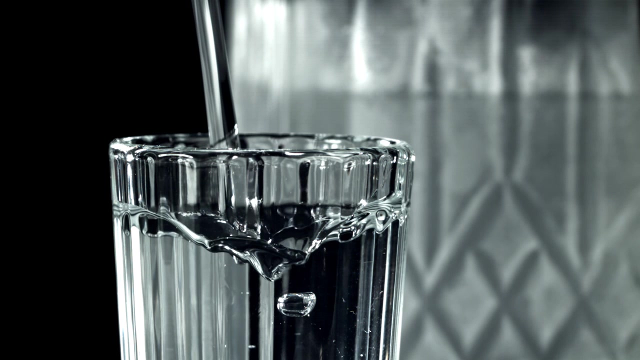 Klart vand hældes i et glas i slowmotion