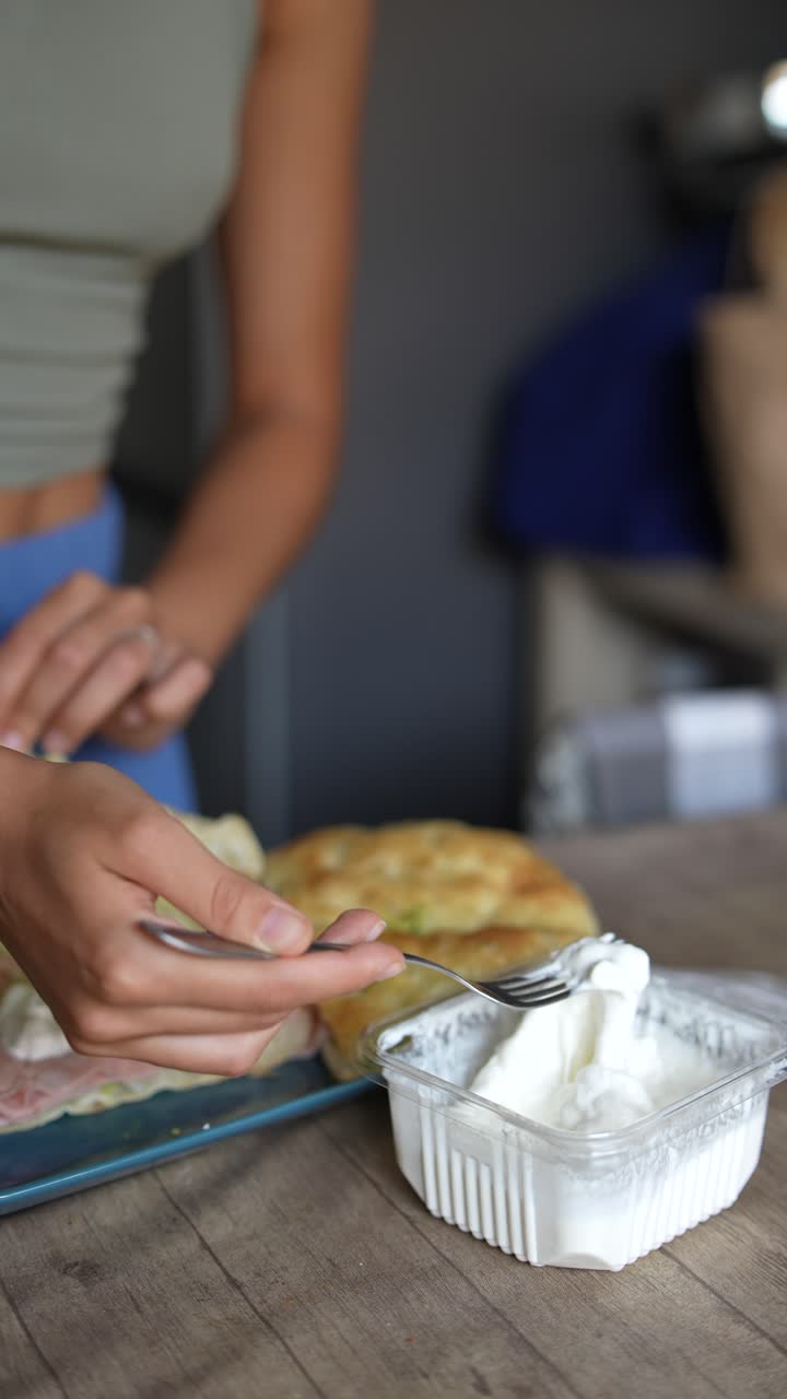 una mujer preparando un sándwich con aguacate, queso cremoso, jamón y mozzarella.