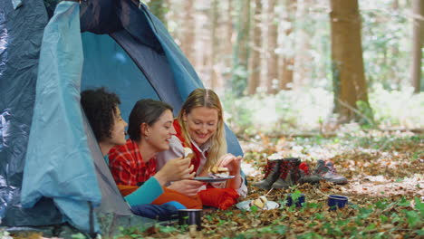 group of female friends on camping holiday in forest lying in tent eating s'mores