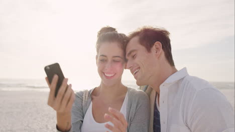 happy couple taking selfies using mobile phone on beach at sunset