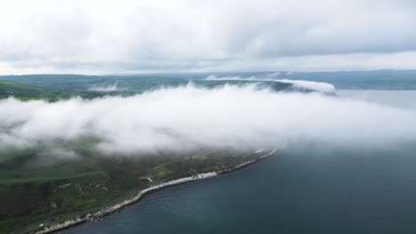 vista aérea por encima de las nubes del hermoso paisaje de irlanda del norte sobre la carretera costera cerca de la ciudad de glenarm con vistas a la tranquila construcción del mar y el paisaje verde