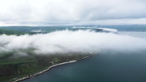 aerial view above the clouds of the beautiful scenery of northern ireland over the coastal road near glenarm town overlooking the calm building sea and green landscape