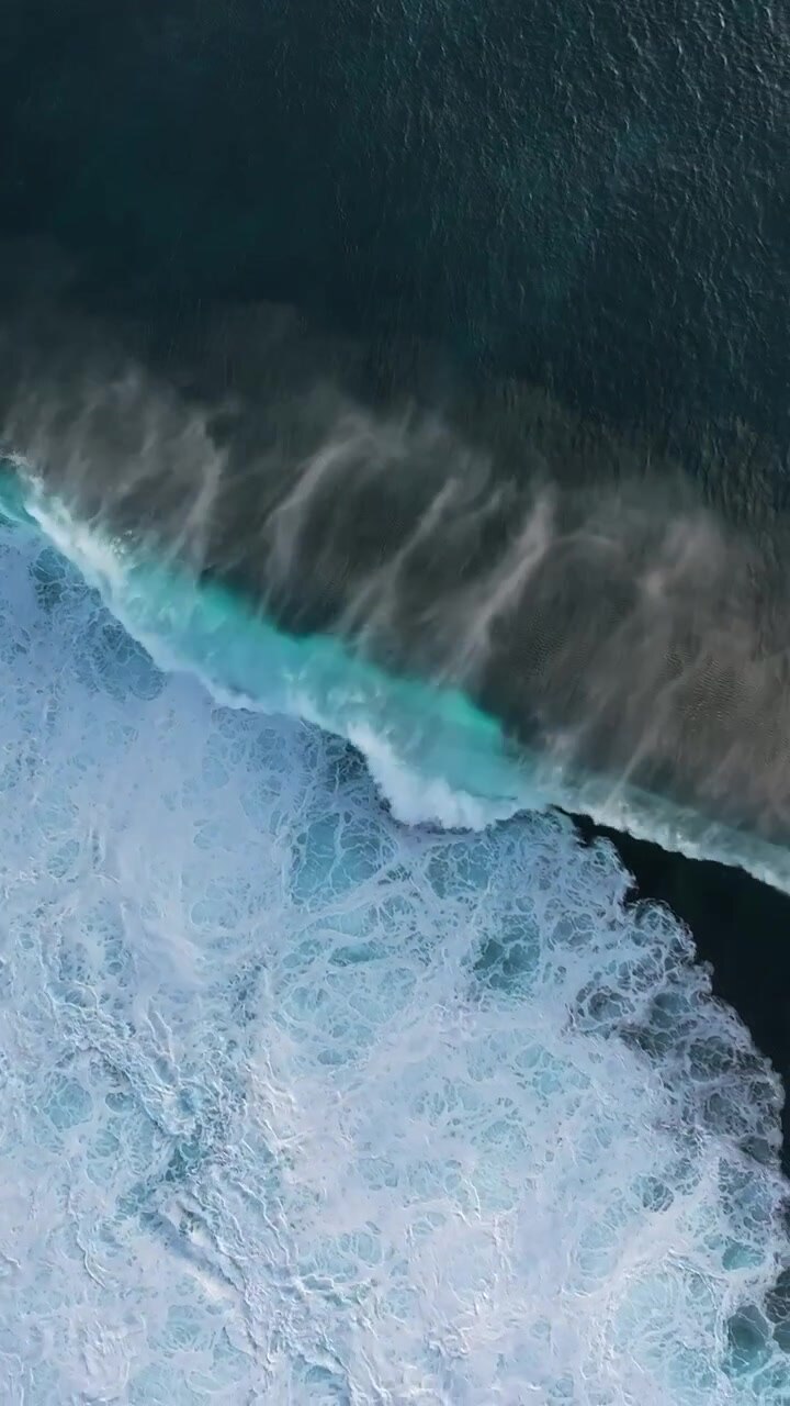 Vibrant turquoise waves crash over a dark coral reef, creating dynamic patterns. Ideal for ocean-themed projects or environmental documentaries.